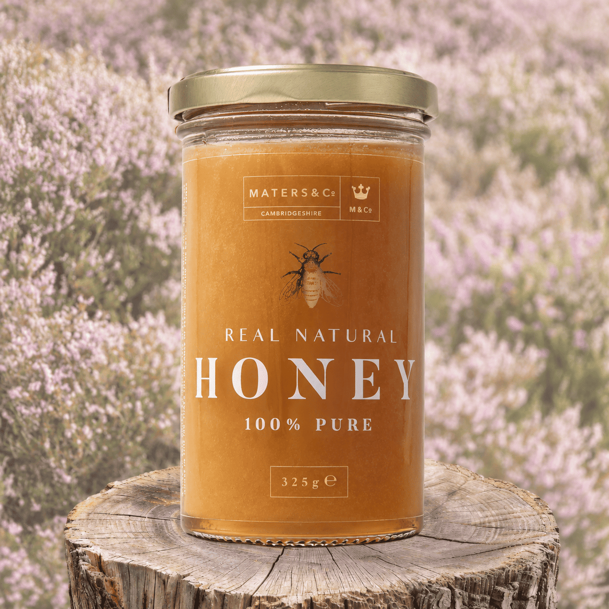 A jar of MATERS & Co Real Natural scottish heather Honey placed on a rustic wooden stump, with a blurred lavender field in the background.