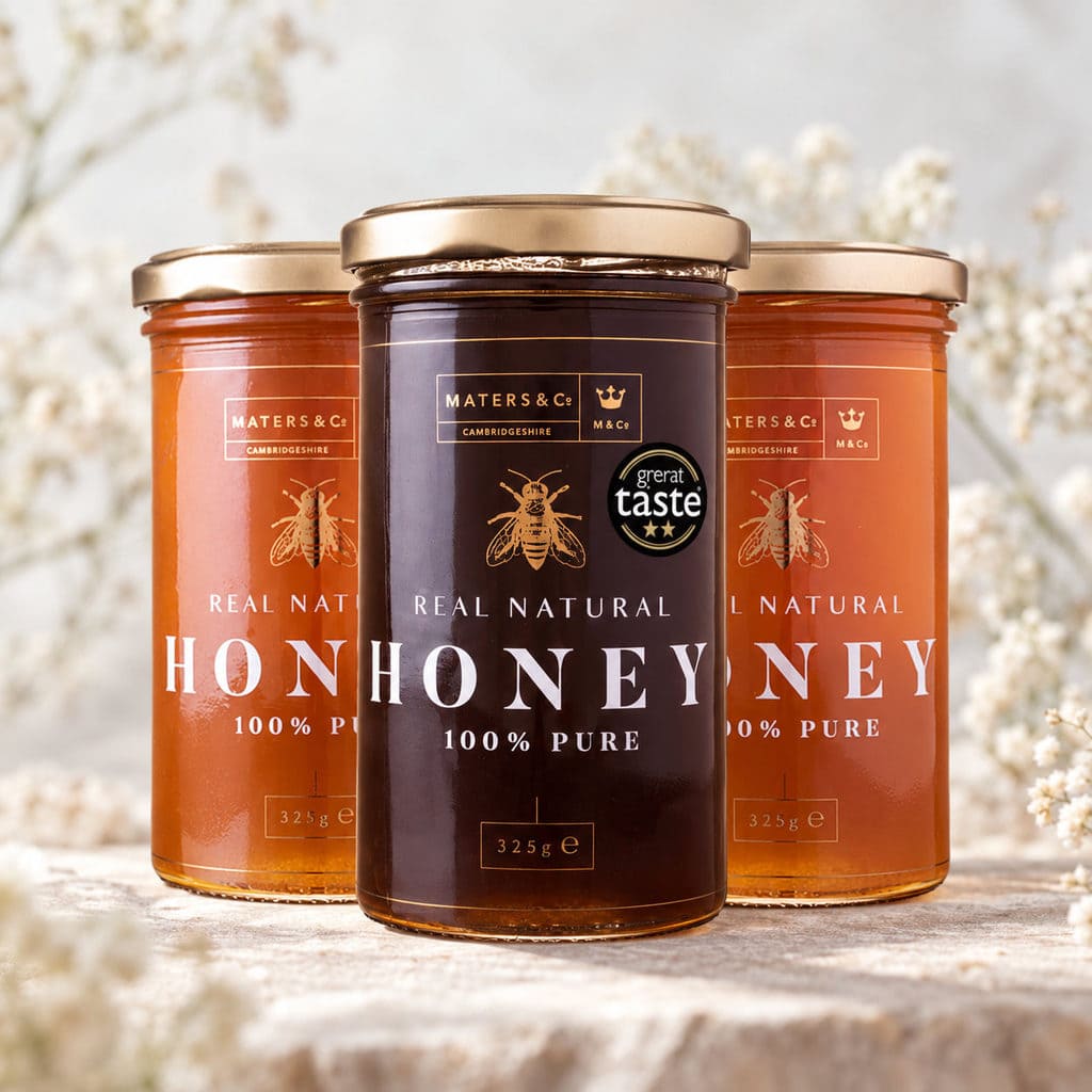 Three glass jars of MATERS & CO. honey arranged in a row, with the center jar in front and a 'great taste' award badge on its label.